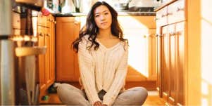 young woman with long dark hair sits on the floor confidently 