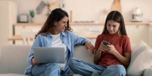 mom and teen daughter on the couch talking while teen looks at phone