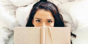 woman lying on bed with book over her face