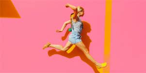 young blonde woman jumping against a pink wall