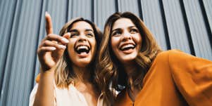 two women laughing in front of a grey wall
