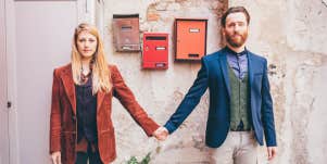 couple in vintage-looking clothing standing in front of a wall with red framed pictures