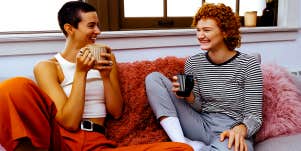two women sitting on couch drinking coffee and chatting