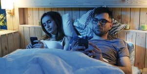 married couple laying in bed looking at their phones