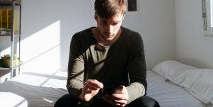 man looking at phone while sitting on bed