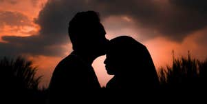 silhouette of man kissing woman's head