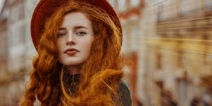 redhead woman with long hair looks at camera, wearing dark red hat