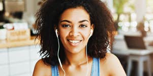 young Black woman smiles in a cafe, wearing earbuds