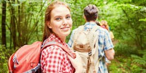 Smiling woman dressed in red hiking through green woods.