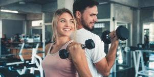 man and woman lifting weights at gym smiling