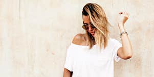 blonde woman in sunglasses, standing against a light wall 