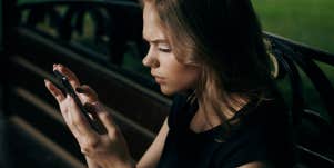 Young beautiful woman is sitting in the phone on a park bench in summer.