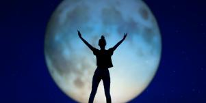 woman standing in front of full moon with arms open