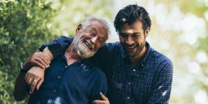 Elderly father with adult son, walking through a grove, arm around the other affectionately 