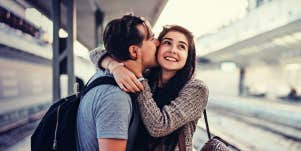 man kissing a woman on a train platform while she laughs 
