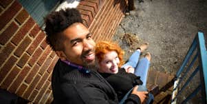 A young couple sit on back door stairs looking back to the camera