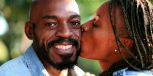 A woman kisses a man on the cheek as he smiles at the camera