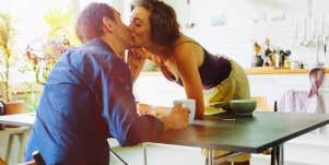 woman leaning over table and kissing man
