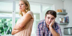 annoyed woman in the kitchen with her back to husband looking resigned