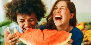 two girls laughing while eating watermelon