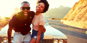 smiling couple standing in front of their car