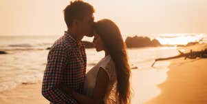 man kissing woman's forehead on beach