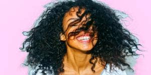 pink background woman smiling with hair in her face