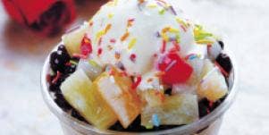 bowl of ice cream with a lot of toppings on table with roses