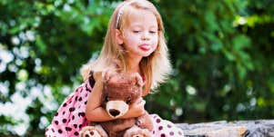 little girl holding teddy bear sticking her tongue out