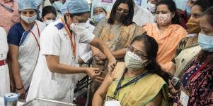 woman getting a vaccine in india while a crowd watches