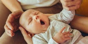 young caucasian baby yawning, held by parents