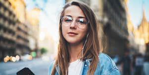 young woman with glasses smiles on a city street