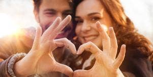 man and woman forming heart with fingers