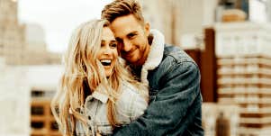 white couple with blonde hair hugs in front of cityscape 