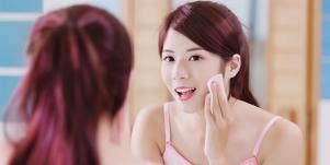 woman putting on makeup in mirror