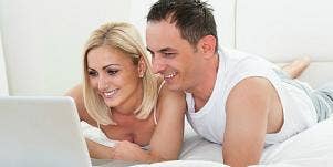 man and woman looking at laptop in bed