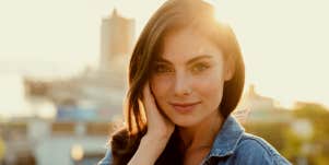 Confident woman smiles with sun behind her.