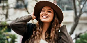 smiling brunette outside in a brimmed hat and jacket