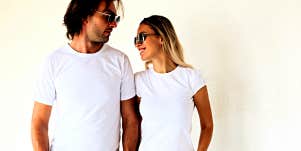 Man and woman look at each other, standing in front of a white wall in white tees 