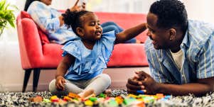 dad laying on floor with young daughter playing with blocks