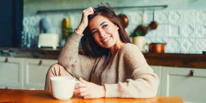Young beautiful asian woman in cozy sweater sitting with cup of tea at table on kitchen at home