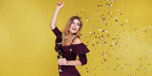 woman celebrating with wine and confetti in front of yellow background