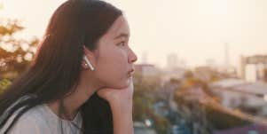 A young woman sits on a rooftop while listening to music