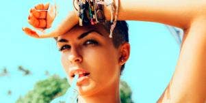 brunette woman against a blue background with her wrist to her forehead, looking into the camera