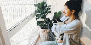 Sensitive woman holding her cat looking out window 