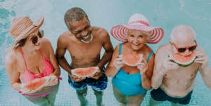 group of older men and women in a pool, looking happy and eating watermelon