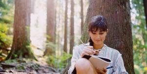 woman writing in a notebook under a tree