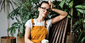 woman in yellow overalls relaxes against a wooden chair by indoor plants