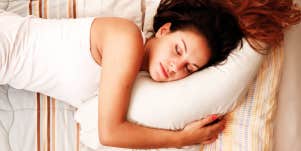 Woman with long brown hair sleeping in bed, hugging a pillow