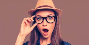 woman wearing a hat and glasses looking at the camera shocked
